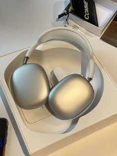 a pair of silver headphones sitting on top of a white table next to a cell phone