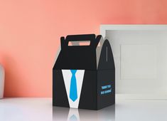 a black box with a blue tie on it next to a white vase and pink wall