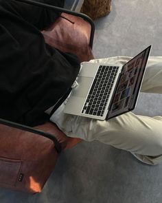 a person sitting in a chair with a laptop on their lap and luggage behind them