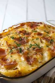 a casserole dish with cheese, ham and parsley in it on a wooden table