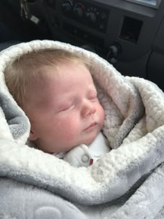 a baby is sleeping in a car seat covered with a blanket and she has her eyes closed