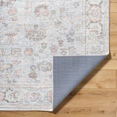 an area rug with blue and beige colors on top of wooden flooring, next to a large piece of furniture