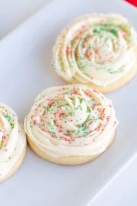 four cookies with white frosting and colorful sprinkles on a plate, ready to be eaten