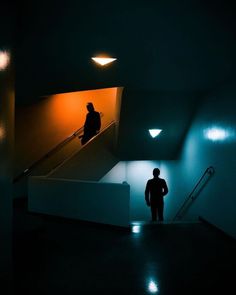 two people are walking up an escalator in a dark room with light coming from the ceiling