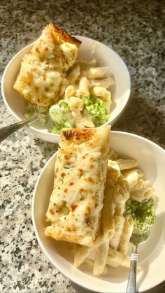 two white bowls filled with pasta and broccoli on top of a marble counter