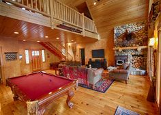 a pool table in the middle of a living room with stairs leading up to an upper level