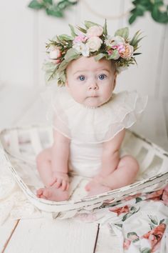 a baby sitting in a basket wearing a flower crown