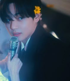 a man in a tuxedo holding a microphone with a flower in his hair