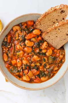 a bowl filled with beans and bread on top of a white counter next to a glass of wine