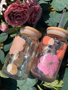 two glass jars with hearts on them sitting next to flowers