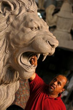 a man is working on a statue of a lion's head with it's mouth open