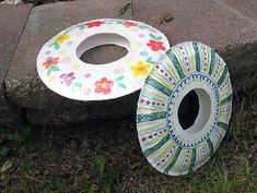 two paper plates sitting next to each other on the ground in front of a rock