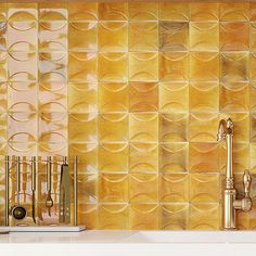 a kitchen counter with gold colored tiles on the wall and utensils next to it