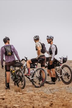 three men standing next to each other with their bikes on the dirt ground in front of them