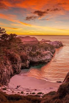 an orange and pink sunset over the ocean with rocky cliffs on one side and water in the other