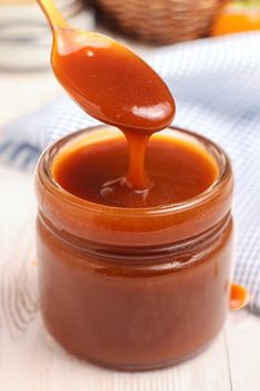 a spoon full of caramel sauce sitting on top of a jar