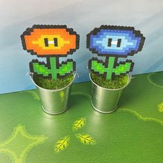 two tin cans filled with flowers on top of a green table