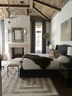 a bedroom with a bed, fireplace and chandelier hanging from the wooden ceiling