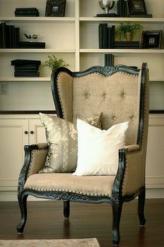 a chair with some pillows on it in front of a book shelf and bookshelf