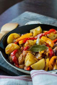 a skillet filled with meat and vegetables on top of a table next to a wooden spoon