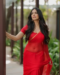 a woman in a red sari posing for the camera with her hand on her hip