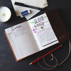 an open notebook sitting on top of a table next to a candle and some pens