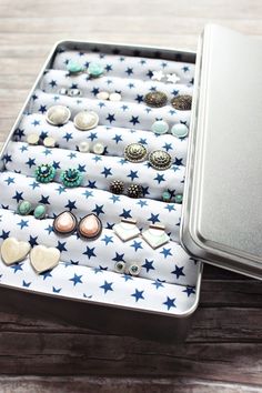 an open tin with several pairs of earring and studs in it on a wooden table