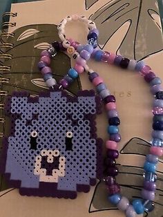 a beaded bookmark with a purple and blue cat on it next to a notebook