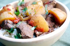 a bowl filled with meat and potatoes on top of rice