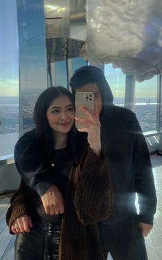 a man and woman taking a selfie in front of a window with the cityscape behind them