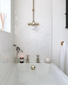 a white bathroom with herringbone tile and gold faucet, along with candles