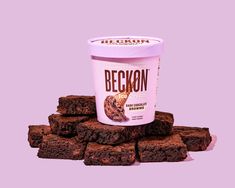 a cup of ice cream sitting on top of some brownie squares in front of a pink background