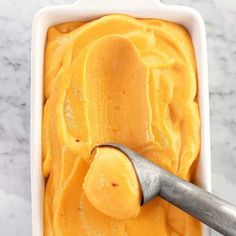 a scoop of mango ice cream in a white dish with a metal spoon on the side