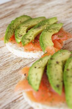 slices of bread with avocado and salmon on them sitting on a wooden table