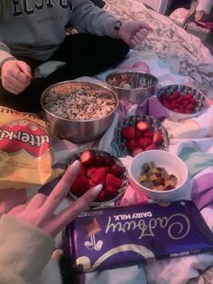 two people sitting on a bed with bowls of cereal and strawberries in front of them