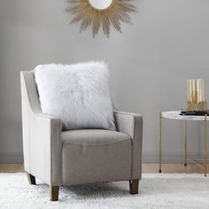 a living room with a chair, table and sunburst mirror on the wall