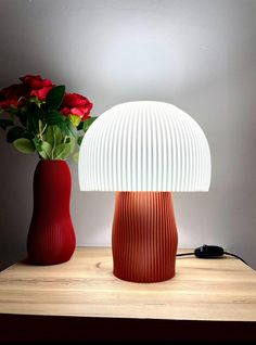 two red vases with flowers in them sitting on a table next to a lamp