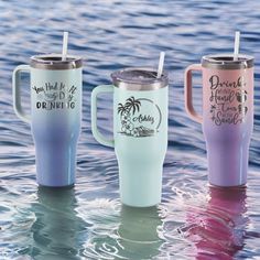 three different colored travel mugs sitting in the water