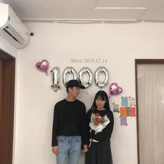 a man and woman standing next to each other in front of balloons on the wall