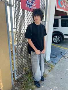 a young boy standing in front of a fence with his hands on his hips and looking at the camera