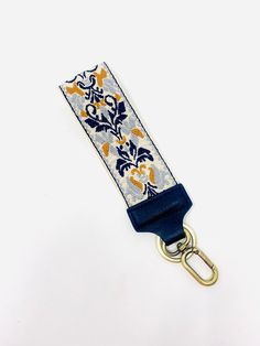 a blue and white lanyard with an orange flower design on the front, hanging from a gold metal hook