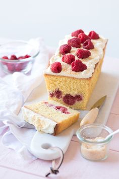 a piece of cake with raspberries and cream frosting next to a knife