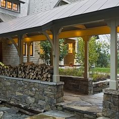 a stone patio with benches and firewood stacked on it