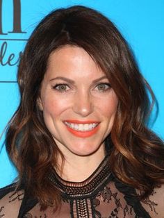 a close up of a person wearing a sheer shirt and orange lipstick smiling at the camera