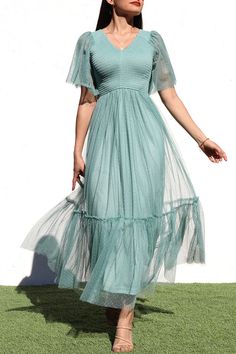 a woman in a blue dress is standing on the grass with her hands out and looking off to the side