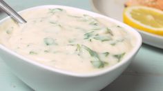 a white bowl filled with soup next to a plate of bread and lemon wedges