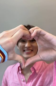 a man making a heart with his hands while wearing a pink shirt and bracelets