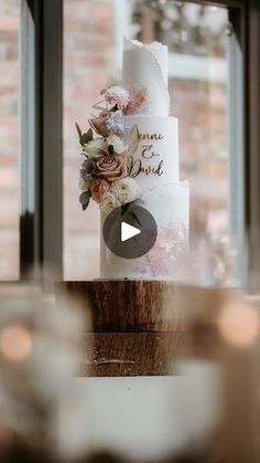 a wedding cake sitting on top of a wooden table in front of a large window