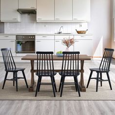 a dining room table with four chairs in front of an open kitchen door and white cabinets