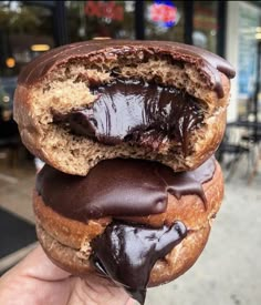 a chocolate covered doughnut being held in front of a storefront with one bite taken out